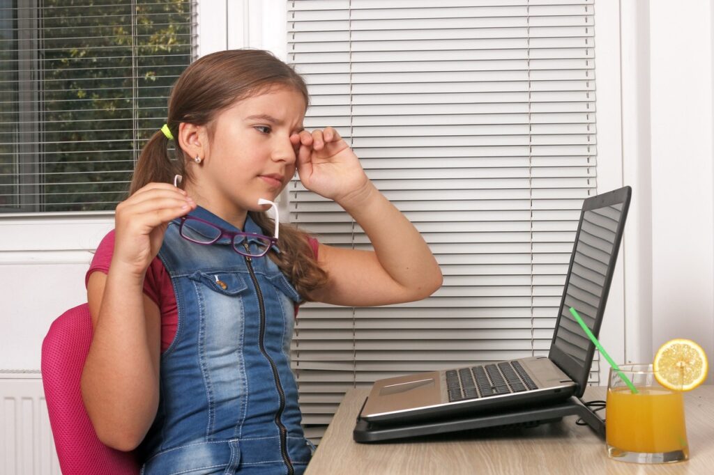 A young child sitting at a desk with a computer, Eye Strain in Children: A Growing Concern