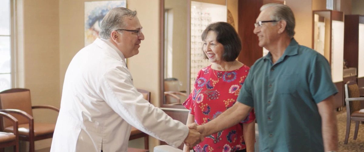 Optometrist shaking hands with a happy couple in an eye care clinic.