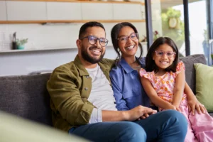 Happy family of three wearing glasses sitting on a couch in a living room.