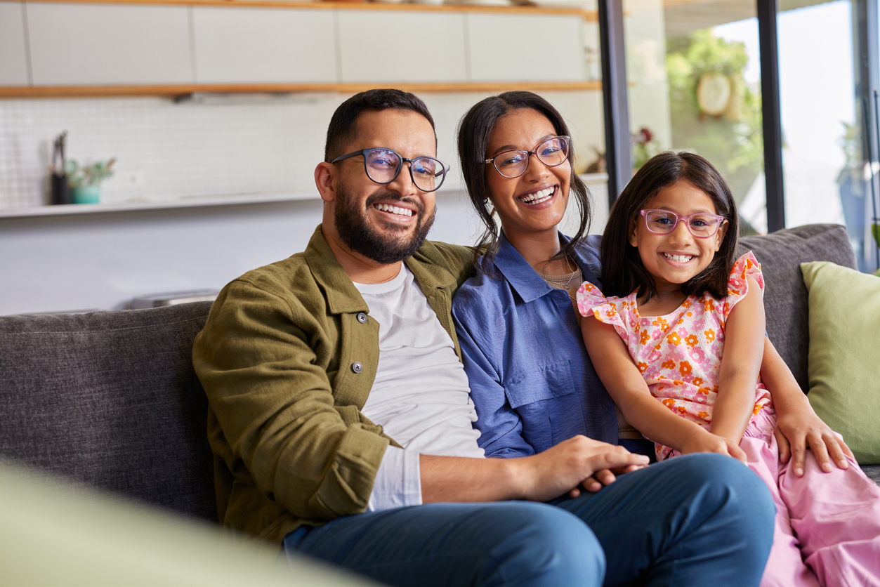 Happy family of three wearing glasses sitting on a couch in a living room.