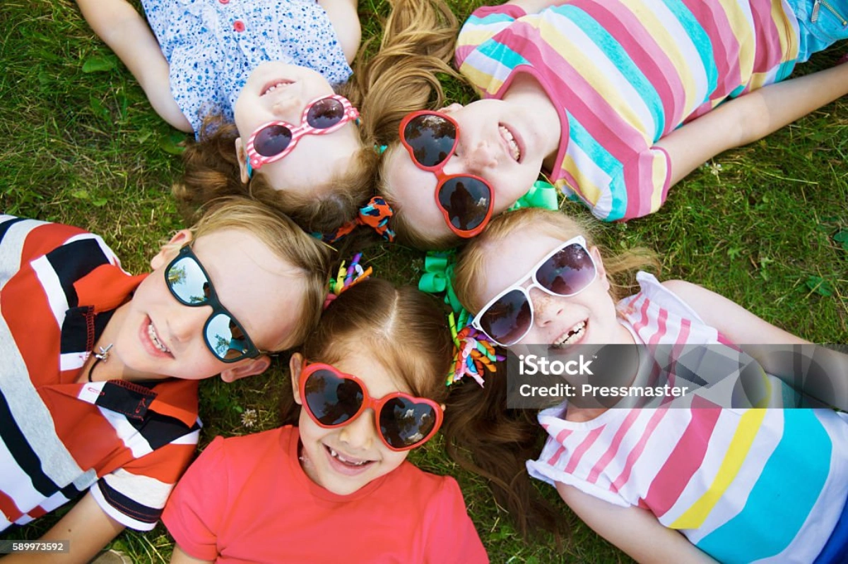 Children lying on grass wearing sunglasses to protect their eyes from UV exposure outdoors