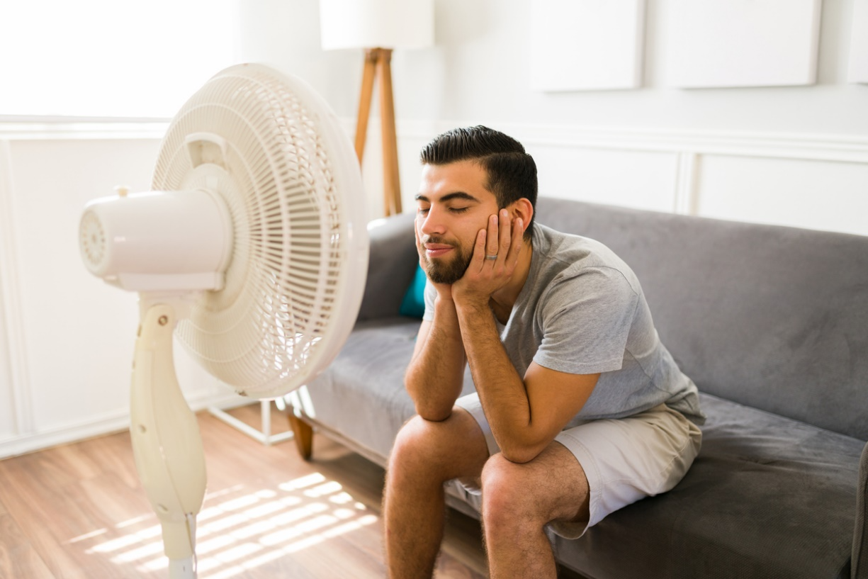Man sitting near a fan indoors during summer, illustrating how airflow and cooling devices can contribute to dry eyes.